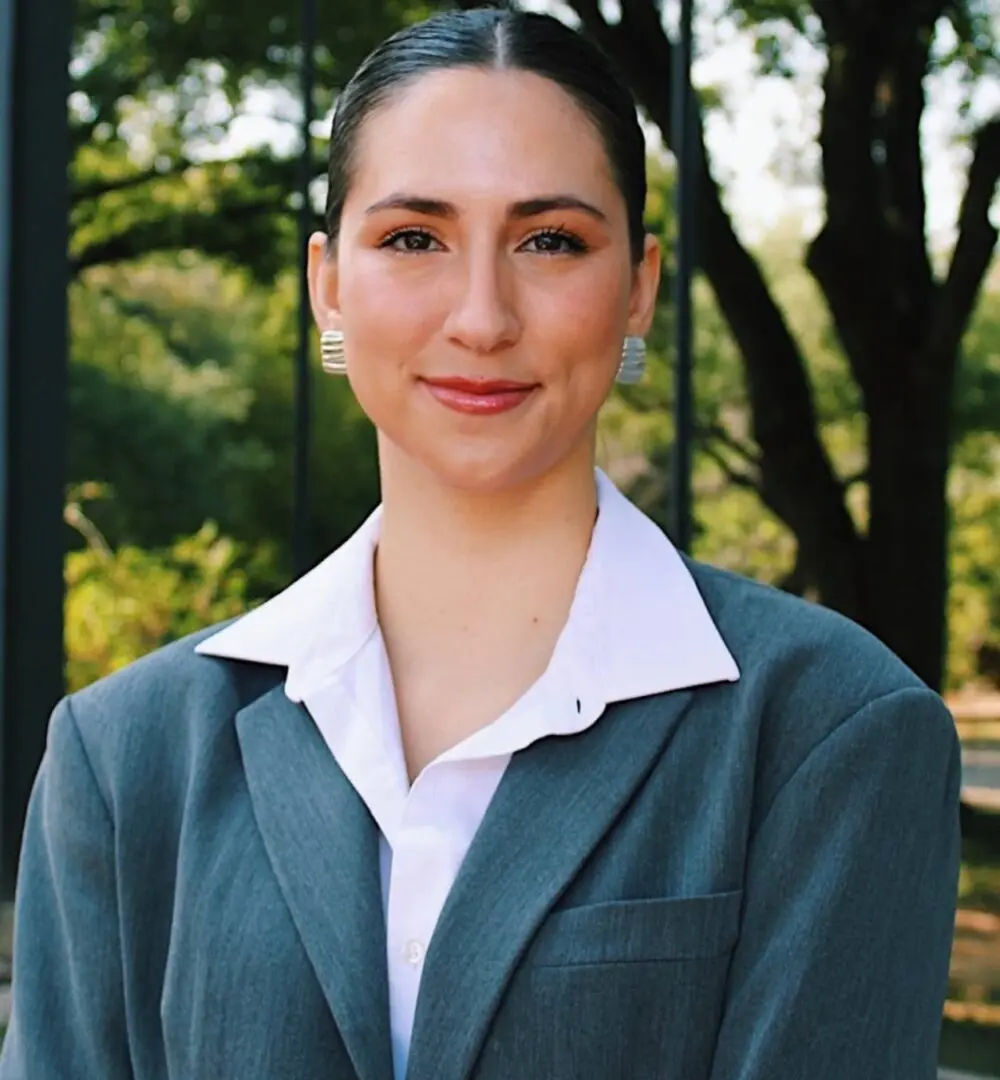 Professional woman in a green suit outdoors with trees in the background.