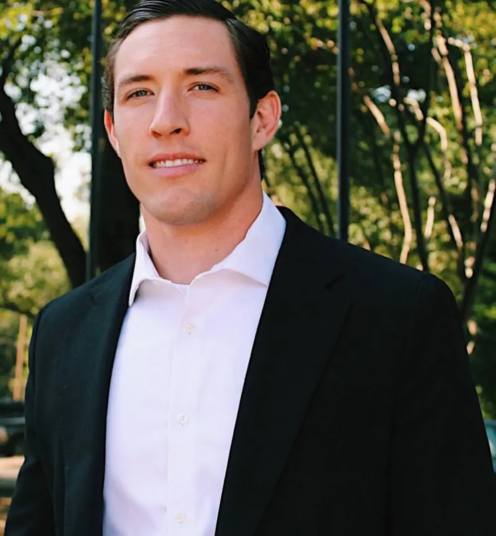 Man in a black suit jacket and white shirt outdoors.